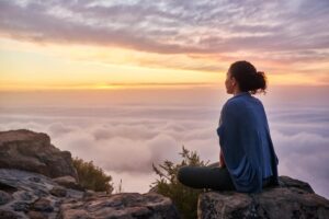 person meditating on mountaintop above the clouds after finding the best treatment for anxiety