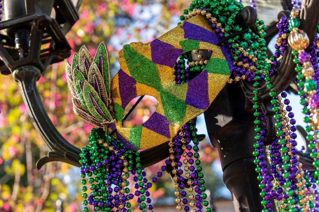 mardi gras mask hanging with beads on lamppost